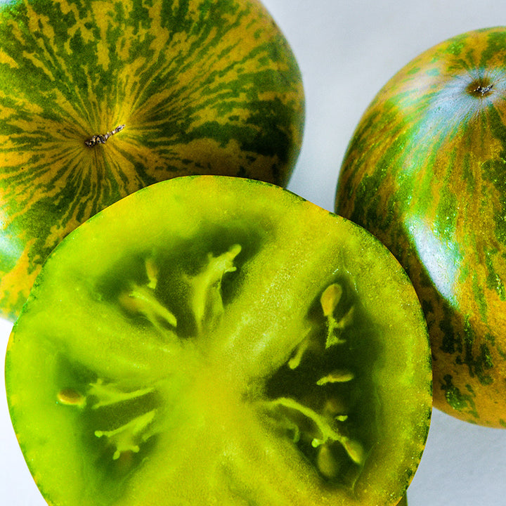 Macro close-up of whole and cut Green Zebra Tomatoes on light background.