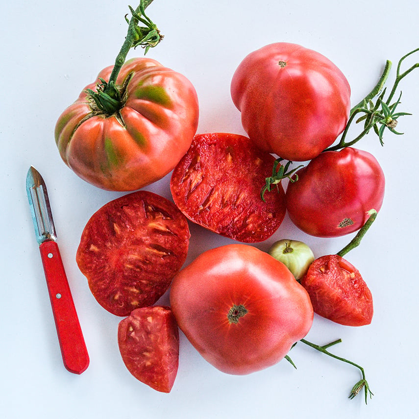 Cut and whole Missouri Pink Love Apple Tomatoes arranged on white background.