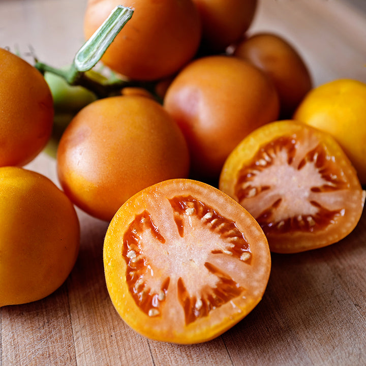 A close-up of cut and whole Orange Peach Tomatoes on light wood cutting board.
