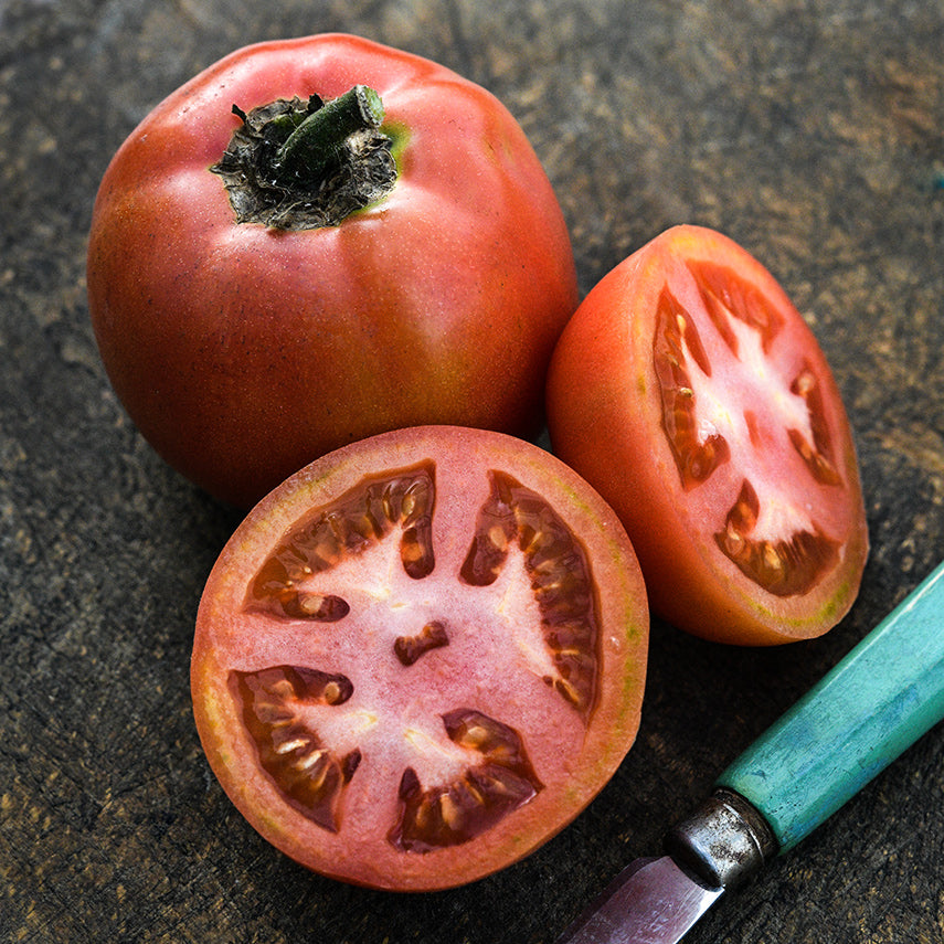 Cut and whole Ozark Pink Tomatoes with a vintage wood handled knife on wooden cutting board.