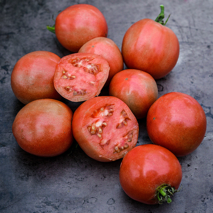 Cut and whole Ozark Pink Tomatoes on brown distressed background.