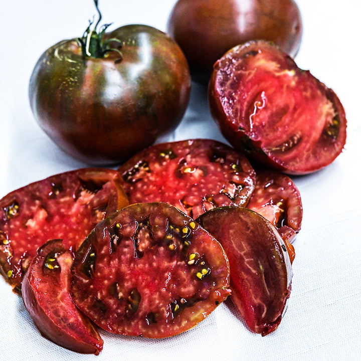 Juicy Paul Robeson Tomato slices with whole tomatoes on linen background.