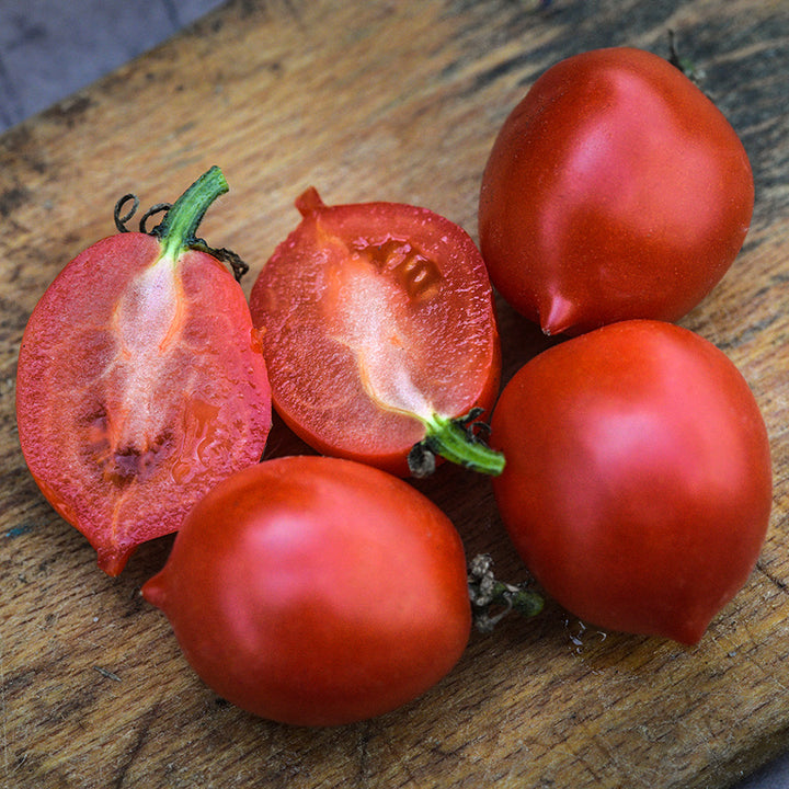 Close-up of cut and whole Principe Borghese Tomatoes on a wooden cutting board.