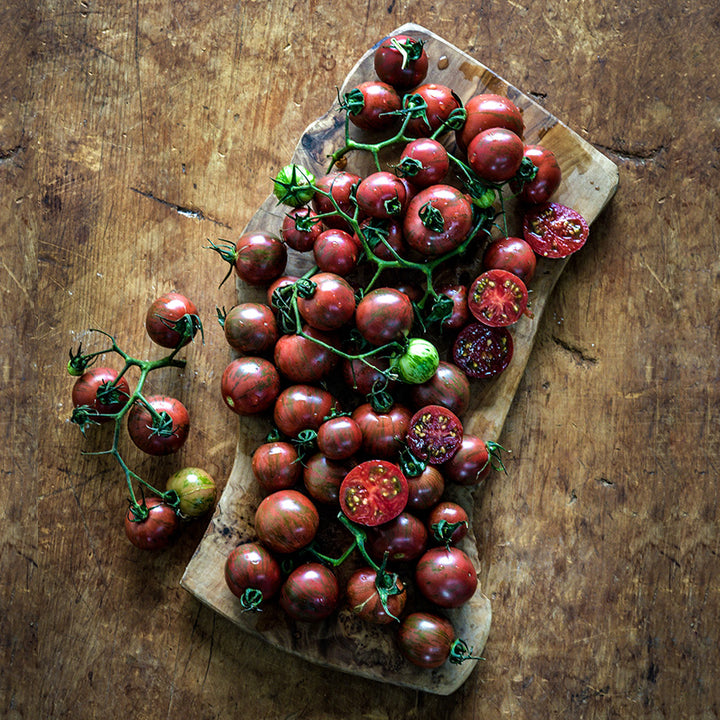 Cut and whole Purple Bumble Bee Tomatoes arranged on wooden background