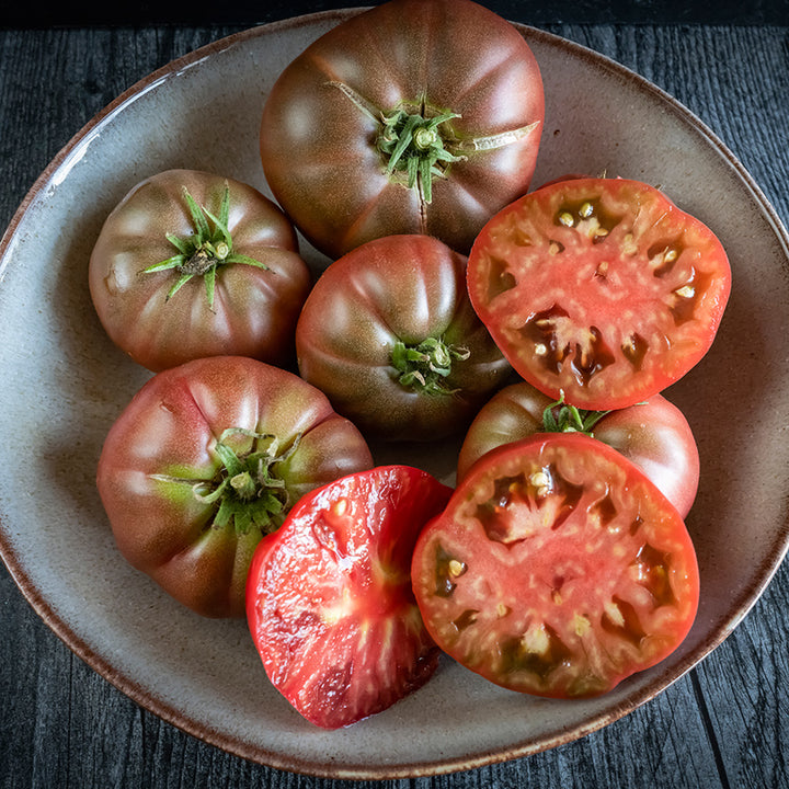 Whole and sliced Purple Reign Tomatoes in a bowl on a gray wood background.