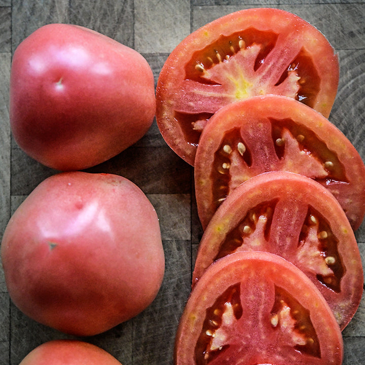 Close-up view of whole and sliced Raspberry Lyanna Tomatoes on a wooden cutting board.