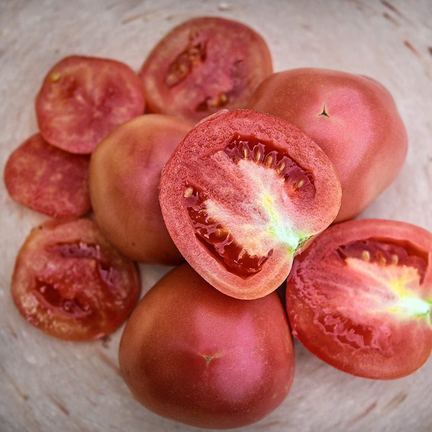 Cut and whole Raspberry Lyanna Tomatoes on a pink terra-cotta plate.