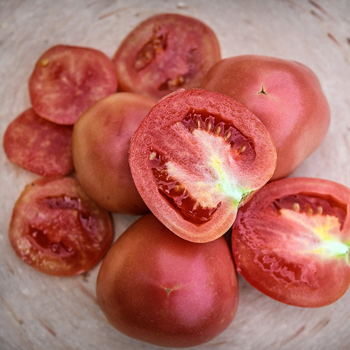 Cut and whole Raspberry Lyanna Tomatoes on a pink terra-cotta plate.