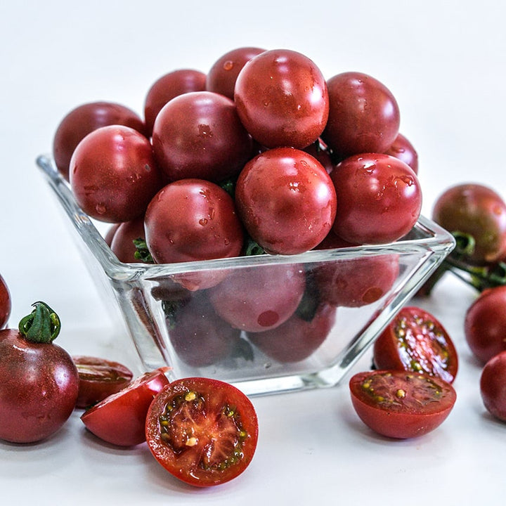 A glass bowl full of Rosella Tomatoes sitting on white background.