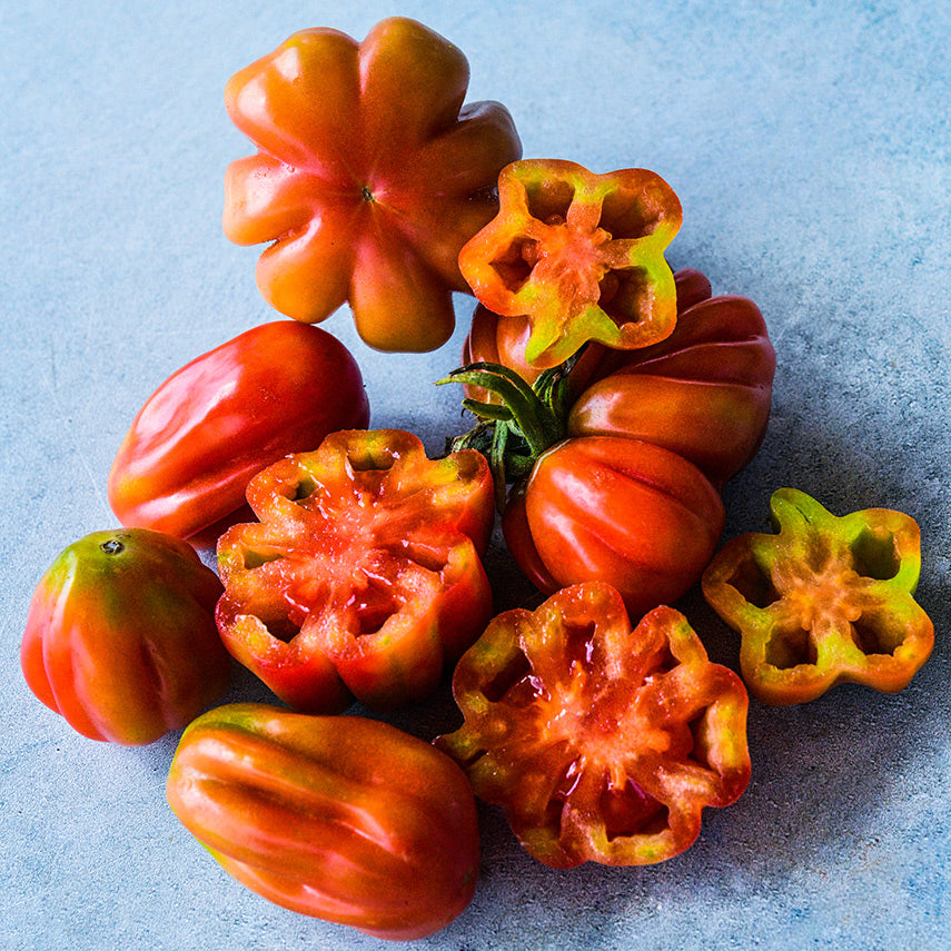 Cut and whole Tlacolula Pink Tomatoes at different stages of maturity showing some yellow.