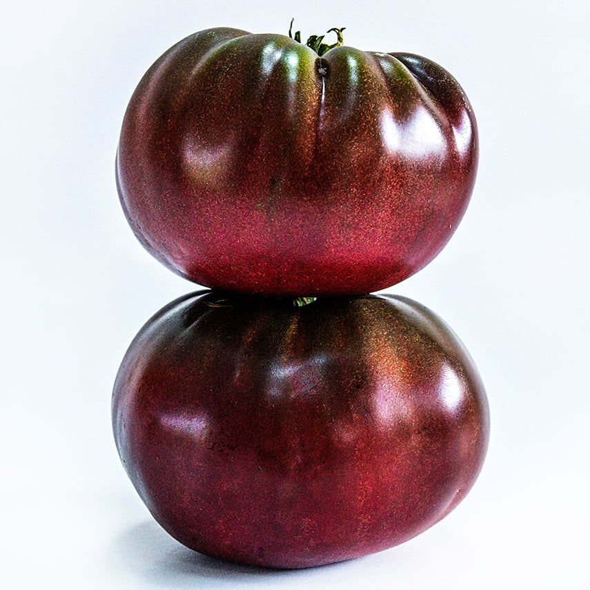 A couple of True Black Brandywine Tomatoes stacked on a white background.