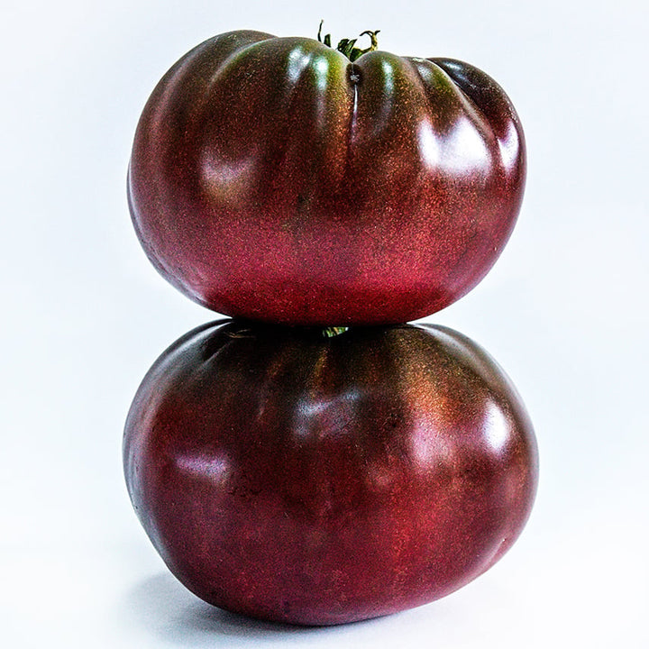 A couple of True Black Brandywine Tomatoes stacked on a white background.