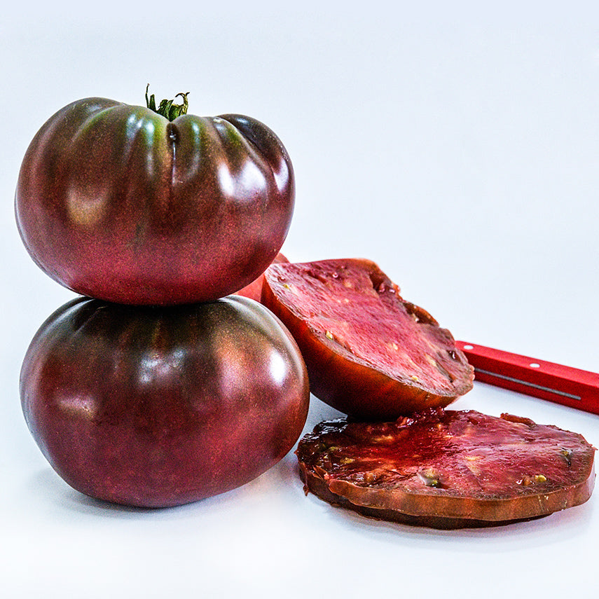 A duo of True Black Brandywine Tomatoes with slices and knife on white background.