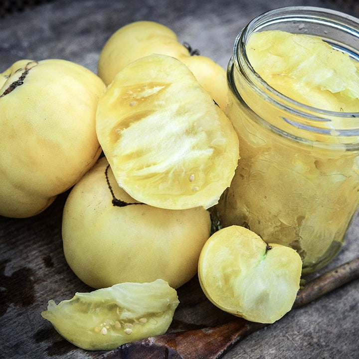 Cut and whole White Tomesol Tomatoes one a wooden cutting board with some cut in a mason jar.