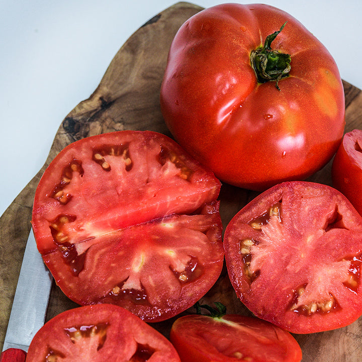 Close-up of cut and whole Wood's Famous Brimmer Tomatoes on wood cutting board.