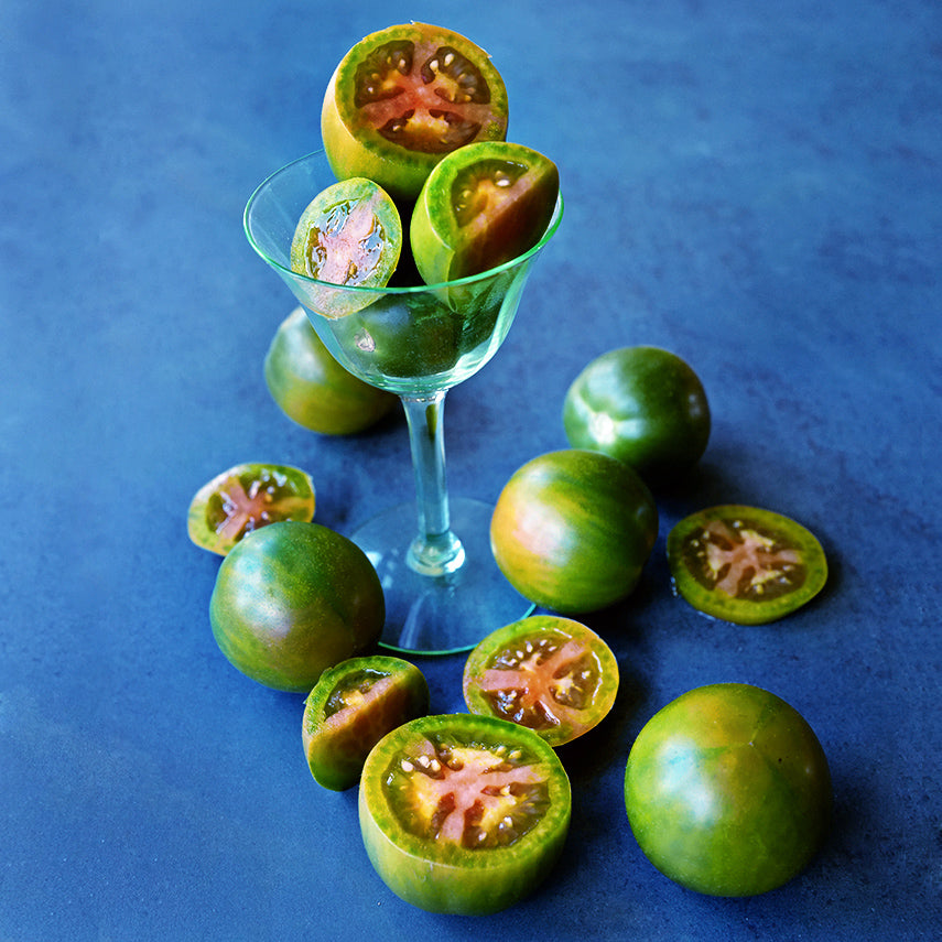 Sliced and whole Evil Olive Tomatoes in a little green martini glass on a dark blue background.