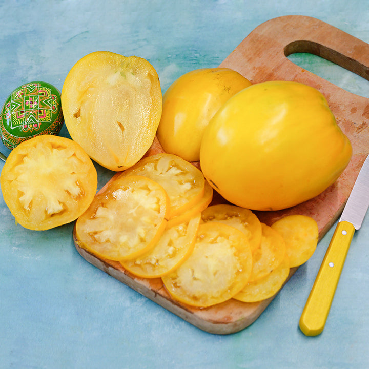 Sliced and whole Golden King of Siberia Tomatoes with a yellow knife and a Russian art decorated egg.