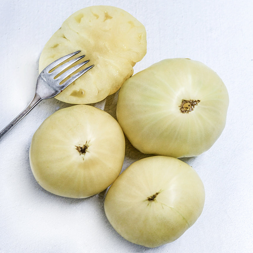 Three whole and a halved Great White Tomatoes with a vintage silver fork on a white background.