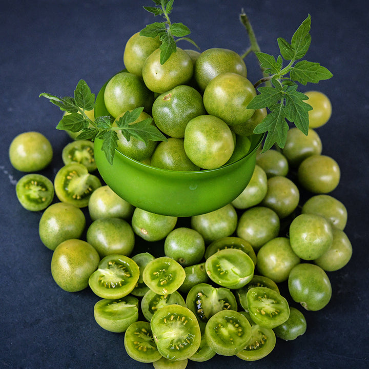 Cut and whole Green Doctors Tomatoes in a green bowl on jade background.
