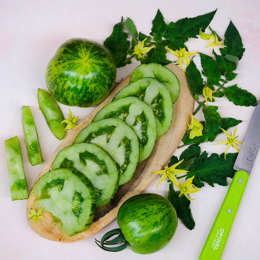 Green Zebra Tomatoes sliced on a wood serving dish surrounded by leaves and blooms.