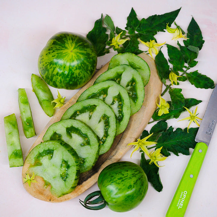 Green Zebra Tomatoes sliced on a wood serving dish surrounded by leaves and blooms.