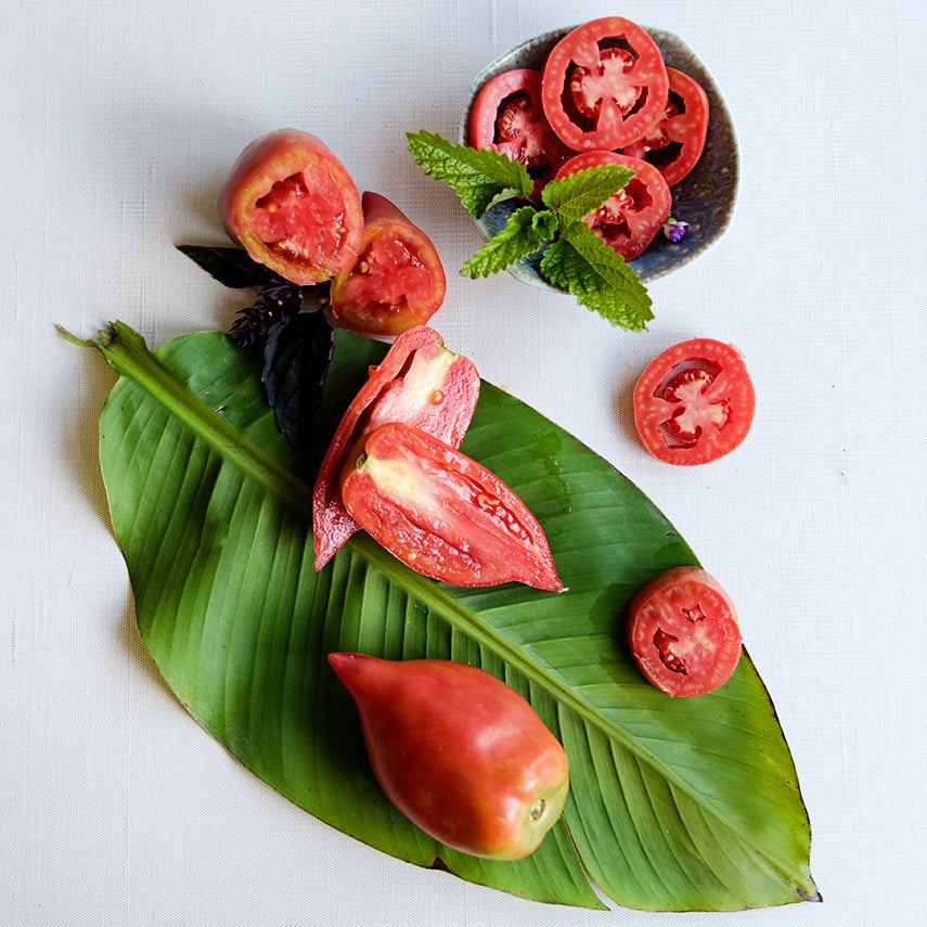 Sliced and whole Korean Long Tomatoes on a large leaf on a linen background.