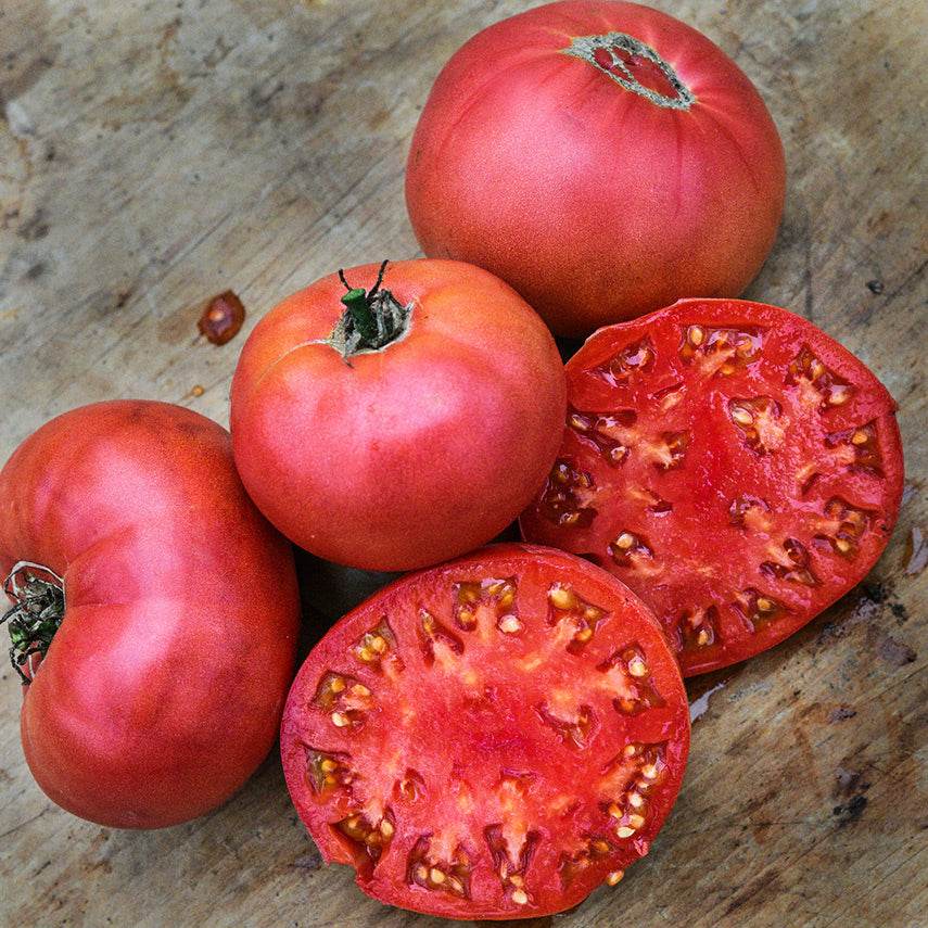 Whole and halved Millionaire Tomatoes on wooden cutting board.