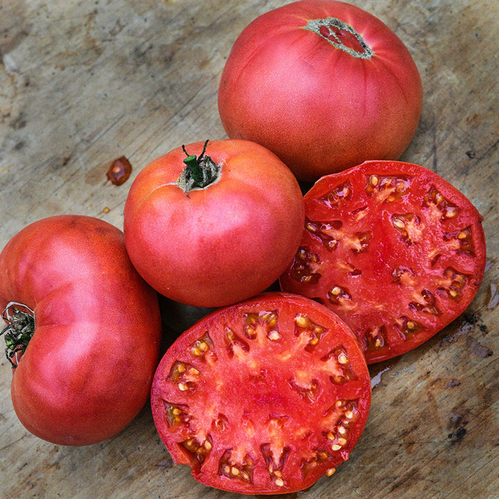 Whole and halved Millionaire Tomatoes on wooden cutting board.