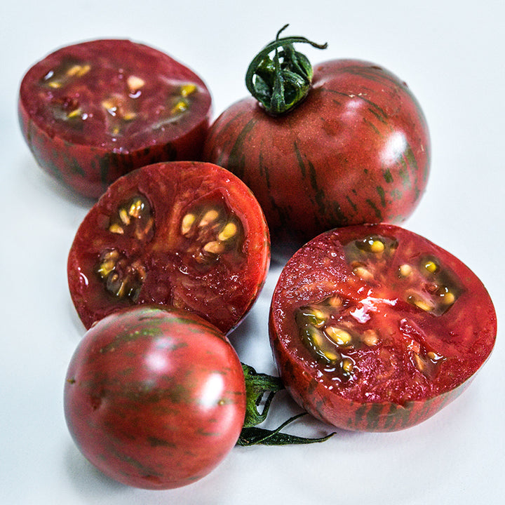 A close-up macro view of cut and whole Purple Bumble Bee Tomatoes on a white background.