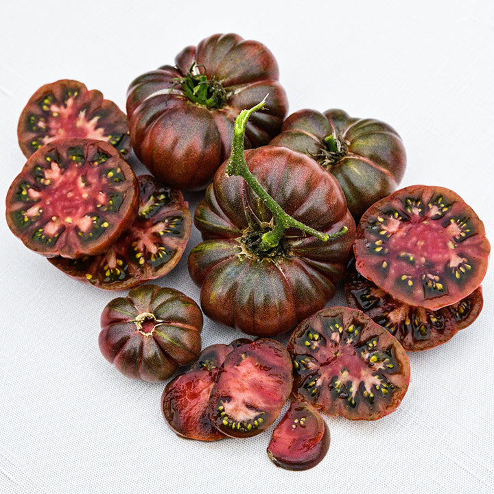 A cluster of sliced and whole Purple Calabash Tomatoes on linen background.