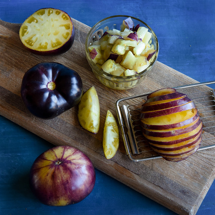 Sliced, cut and whole Sart Roloise Tomatoes on a cutting board against a deep blue background.
