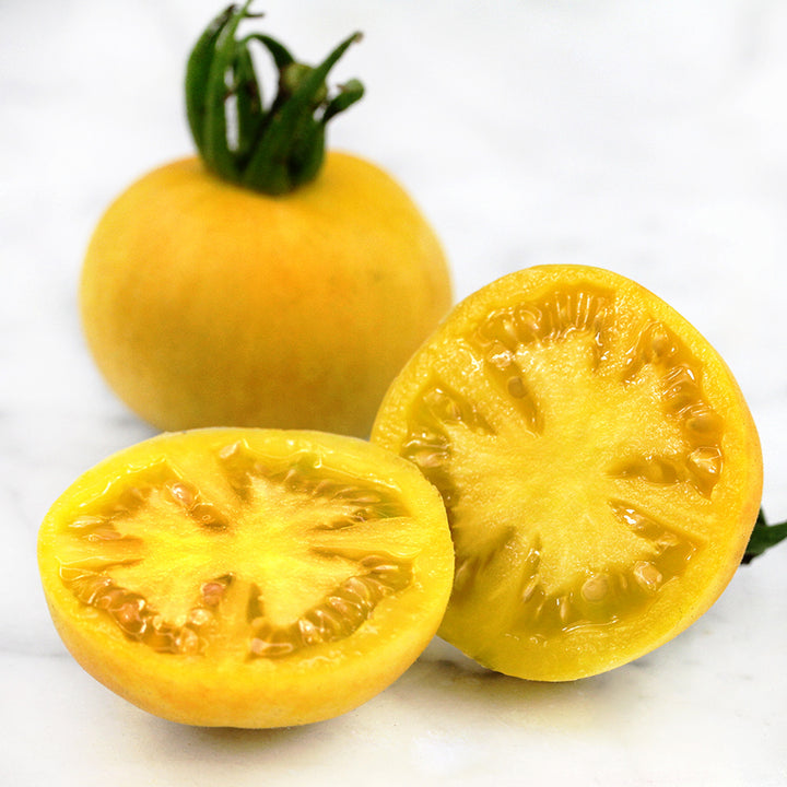 One sliced and one whole Wapsipinicon Peach Tomatoes on a white marble counter.