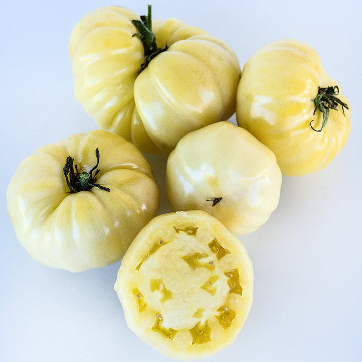 Cut and whole White Beauty or Snowball Tomatoes on a white background.