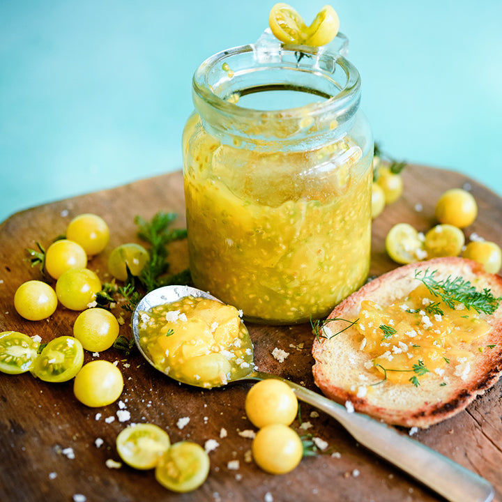 Close-up view of sweet White Currant Tomato Jam with some on toast displayed on wood cutting board.