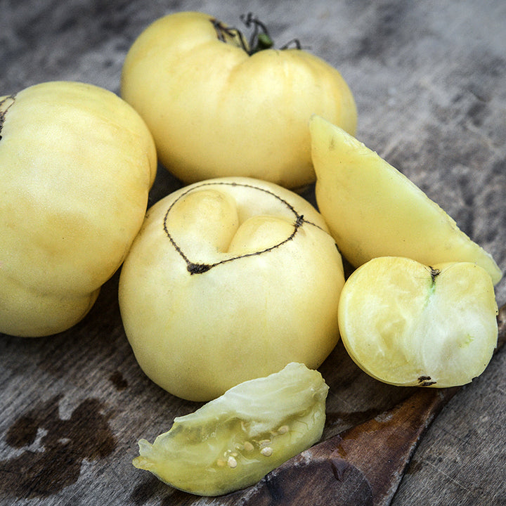 Sliced and whole White Tomesol Tomatoes with a wooden spoon on wood cutting board.