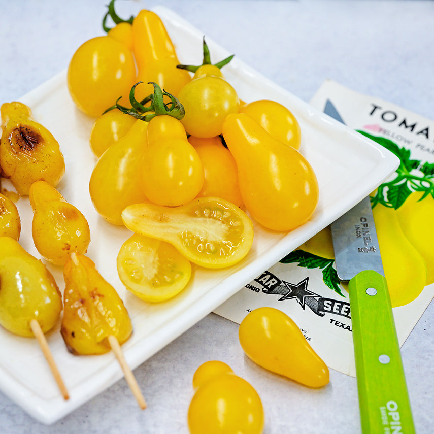 Roasted and fresh Yellow Pear Tomatoes on a white plate with a vintage seed packet and knife.