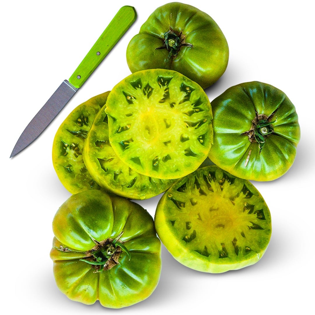 Overhead view of Green Giant Tomato slices surrounded by three tomatoes and a green handled knife on a white background.