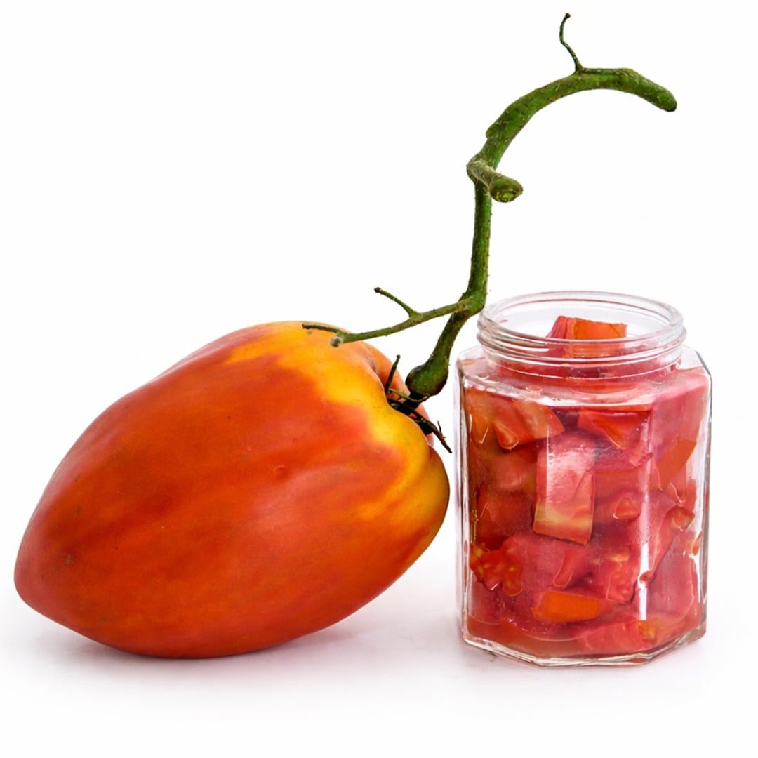 A single Palemeno Tomato with a jar of chopped tomatoes on a white background.