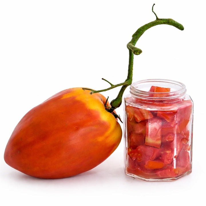 A single Palemeno Tomato with a jar of chopped tomatoes on a white background.