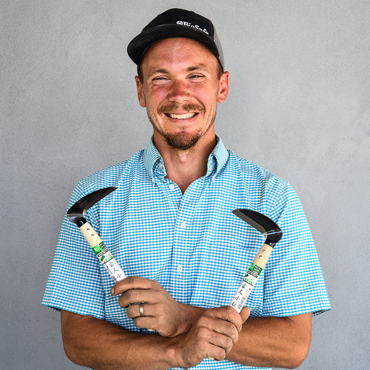 The Baker Creek garden manager smiles as he holds a Left and Right Handed Professional Sickle in each hand.