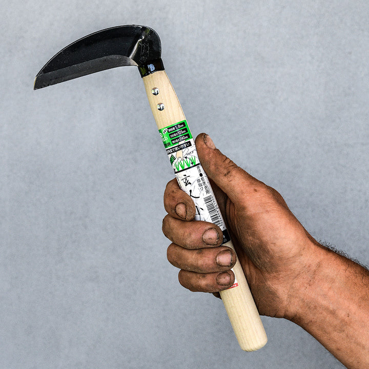 A gardener's hand holding a Professional Sickle Right Handed Tool against a light gray background.
