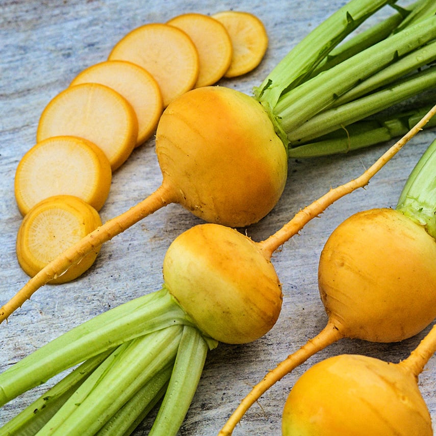 Whole sliced yellow Aji Kogane Turnips on a weathered white wood background.