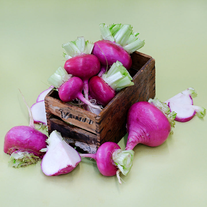 Cut and whole Hida Beni Red Turnips in a wooden box on light green seamless background.