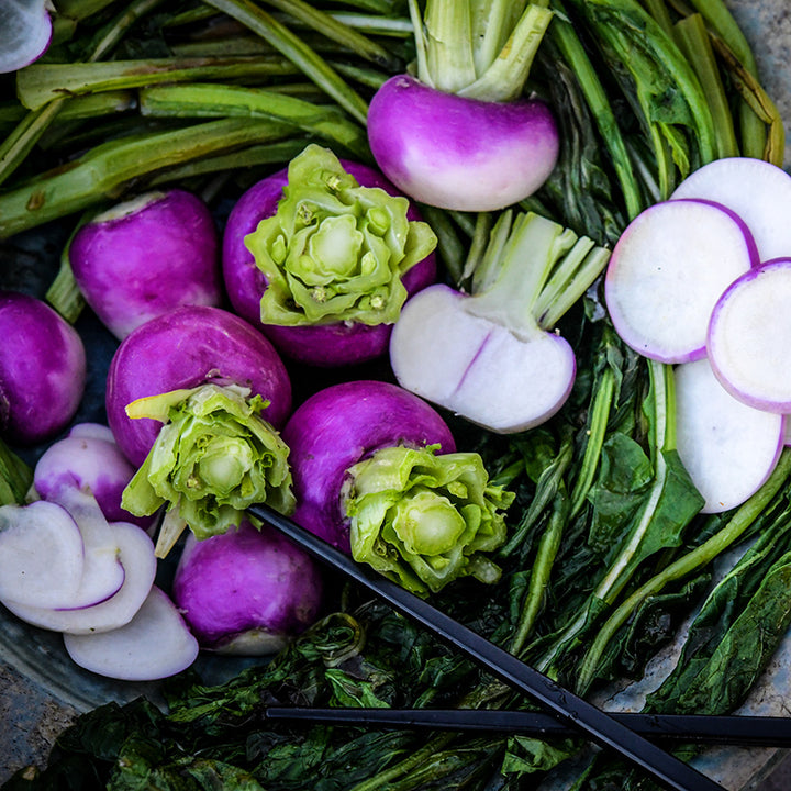 Close-up view of sauteed greens with Nagasaki Akari Kabu turnips in ceramic bowl.