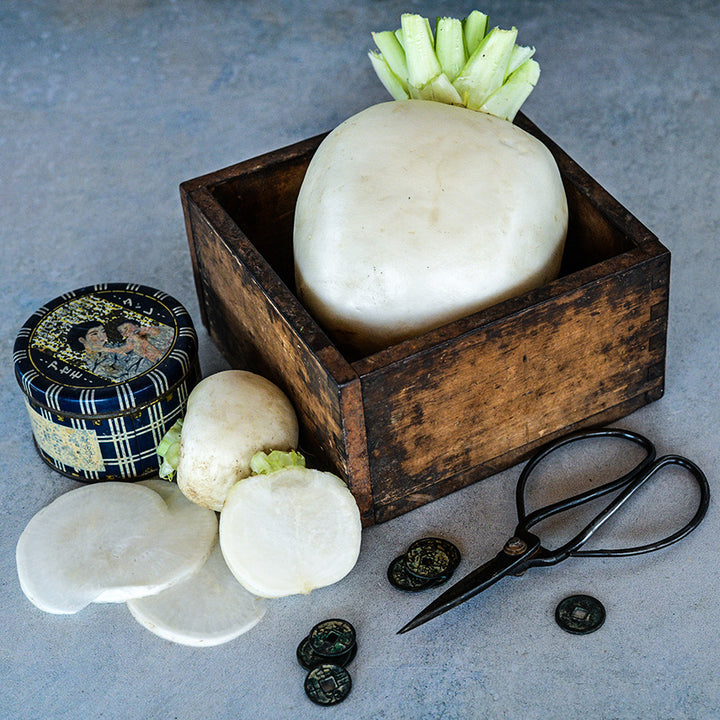 A large Tokinashi Turnip in a wooden box with smaller turnips and Japanese props beside it.