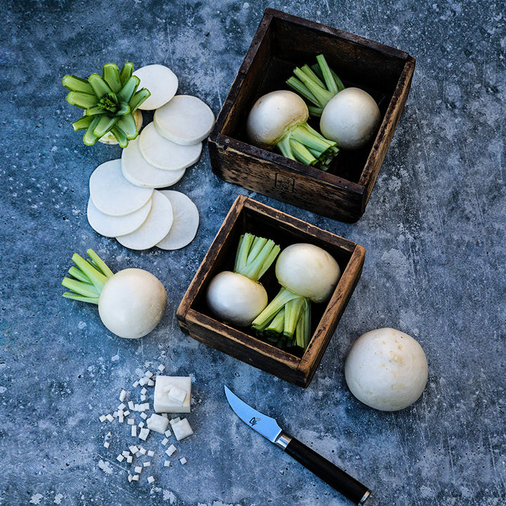 Two wooden boxes holding Tokinashi Turnips with a sliced turnip beside them on a grey background.