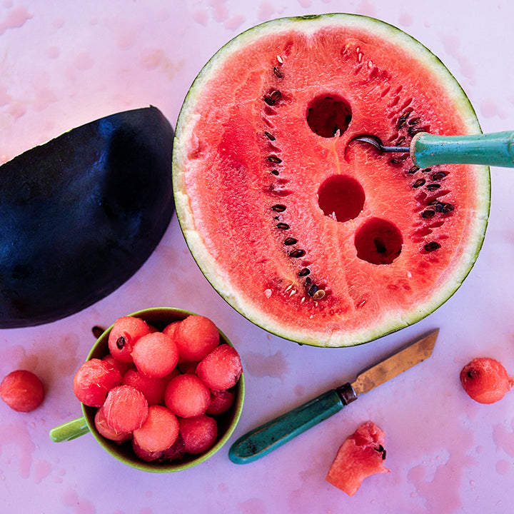 A cut up Blacktail Mountain Watermelon with melon balls on a pink background.
