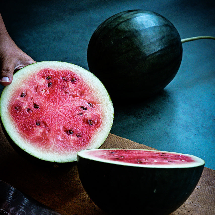 Woman cutting a Blacktail Mountain Watermelon on cutting board with a whole melon in the background.