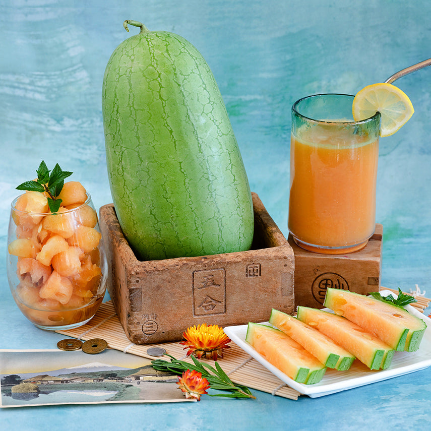 A whole Kaho Watermelon surrounded by slices, melon balls and watermelon juice.