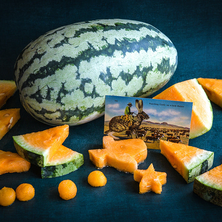 A whole Orangeglo Watermelon surrounded by slices in the shape of Texas and a giant Jackrabbit postcard.